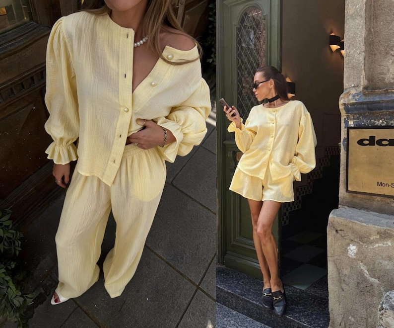 May include: A light yellow two-piece set consisting of a long-sleeved button-down shirt with gathered cuffs and matching wide-leg trousers. The shirt features a round neckline and pearl-like buttons, while the trousers have a relaxed fit.