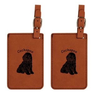 May include: Two brown leather luggage tags with a black silhouette of a Cockapoo dog and the word "Cockapoo" engraved on each tag.