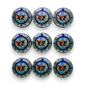 May include: Nine round, colorful, glass ornaments with a stained glass design featuring a crab with the Maryland state flag on its shell. The crab is surrounded by a blue circle with yellow and green accents.