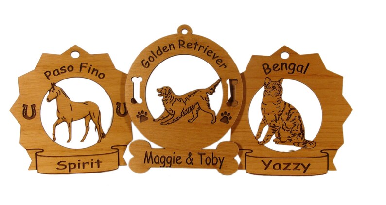 K&ouml;nnte beinhalten: Drei Holzornamente mit lasergravierten Bildern eines Pferdes, eines Golden Retrievers und einer Bengal-Katze. Die Ornamente sind mit den Namen "Spirit", "Maggie & Toby" und "Yazzy" verziert.