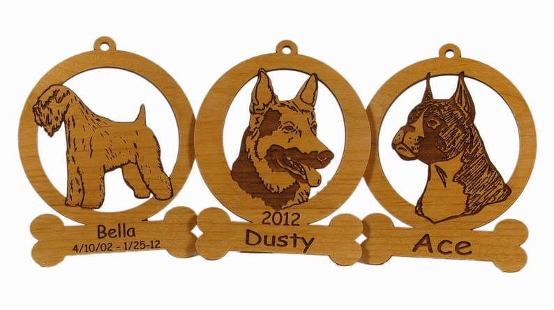 May include: Three wooden dog ornaments with engraved portraits of dogs and their names. The ornaments are attached to a bone-shaped piece with the text "Bella 4/10/02 - 1/25-12", "2012 Dusty", and "Ace".