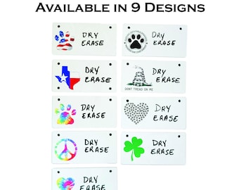 May include: Nine different designs of 5 x 2.5 inch dry erase crate tags. Each tag features a different graphic, including a peace sign, a heart, a shamrock, a paw print, a snake, a Texas flag, and an American flag. The text "DRY ERASE" is written on each tag.