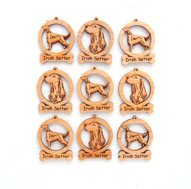 May include: Nine wooden Irish Setter ornaments. Each ornament features a laser-cut dog design within a circular frame. The words "Irish Setter" are laser-cut on a bone-shaped tag below each ornament. The ornaments are light brown.