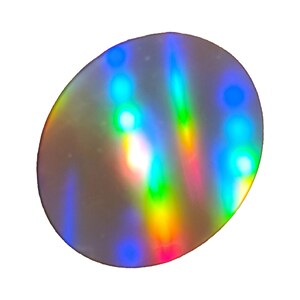 May include: A reflective, iridescent disc with a silver base. The surface displays a spectrum of colors, including blue, green, yellow, and red, creating a rainbow effect. The disc is circular with a slightly oval shape.