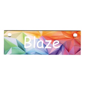 May include: A colorful rectangular tag with a geometric pattern in shades of orange, yellow, green, blue, and purple. The tag has two holes punched in the top corners and the word "Blaze" written in white in the center.