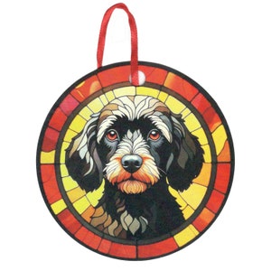 May include: A round, stained glass ornament featuring a black and white dog with brown accents. The dog's face is centered in the ornament, with a red, yellow, and orange stained glass background.