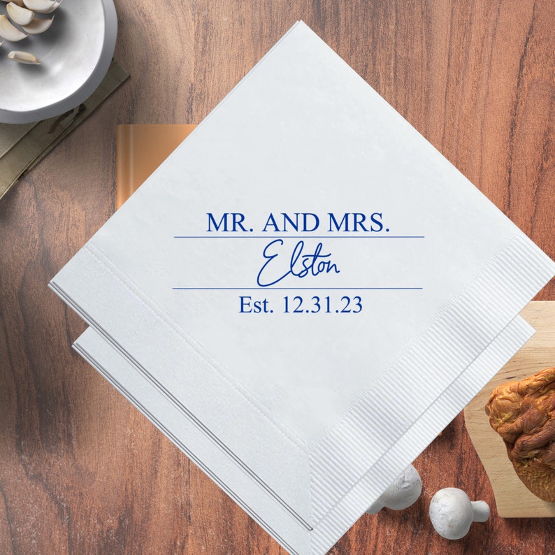 May include: White paper napkins with blue text that reads "MR. AND MRS. Elston Est. 12.31.23".
