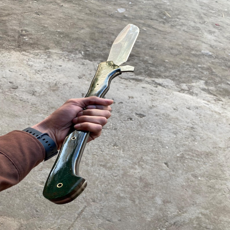 Op de afbeelding: Een lang mes met een zwart en groene handvat en een zilveren lemmet. Het handvat heeft een decoratief ontwerp en twee messing accenten.
