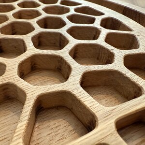 May include: Close-up of a wooden serving tray with a honeycomb design. The tray is made of light-colored wood and features numerous hexagonal cutouts. The edges of the tray are rounded, and the wood grain is visible.