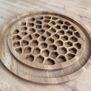 May include: A set of three wooden serving trays. The largest tray has a raised edge, and the middle tray features a honeycomb pattern. The smallest tray is a solid circle. All trays are made of light-colored wood.
