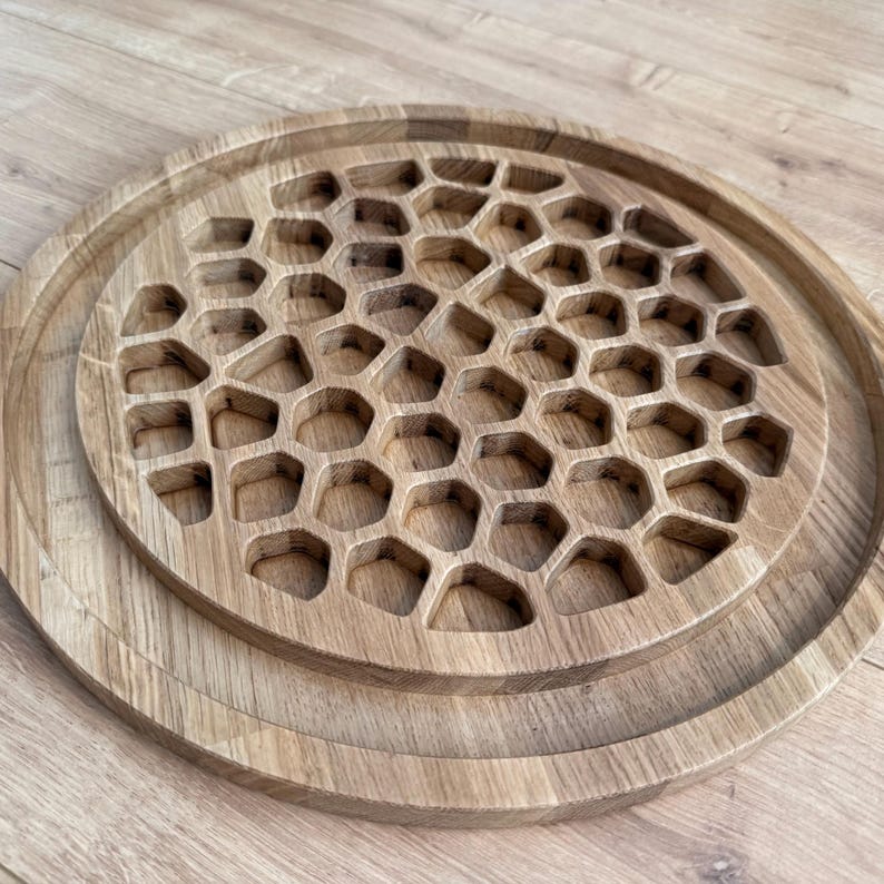 May include: A set of three wooden serving trays. The largest tray has a raised edge, and the middle tray features a honeycomb pattern. The smallest tray is a solid circle. All trays are made of light-colored wood.