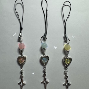 Puede incluir: Tres charms para teléfono con correas negras, charms de corazón plateados y charms de estrella. Las cuentas son rosadas, azules y amarillas.