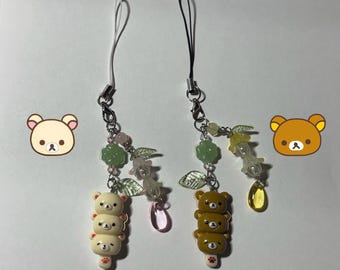 Könnte beinhalten: Zwei dekorative Handy-Anhänger mit gestapelten Bärenfiguren. Ein Anhänger hat hellfarbene Bären, der andere braune Bären. Beide Anhänger haben florale und Blatt-Akzente mit einer tropfenförmigen Perle.
