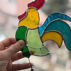 May include: A stained glass rooster with red, yellow, green, and blue glass pieces. The rooster is facing left and has a long tail.