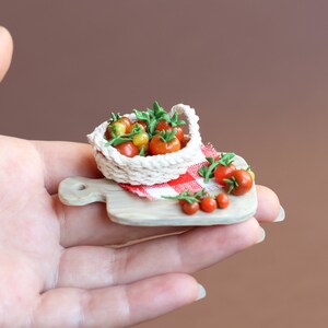 May include: A miniature white crocheted basket filled with red and yellow tomatoes sits on a small wooden cutting board with a red and white checkered cloth. A few more tomatoes are scattered around the basket.