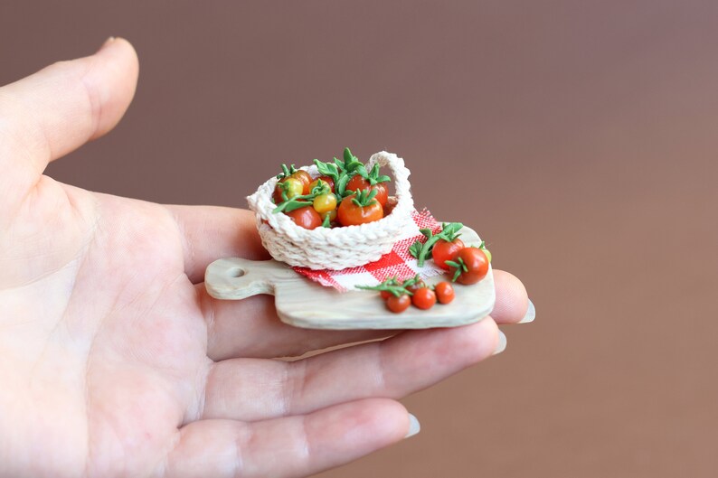 May include: A miniature white crocheted basket filled with red and yellow tomatoes sits on a small wooden cutting board with a red and white checkered cloth. A few more tomatoes are scattered around the basket.