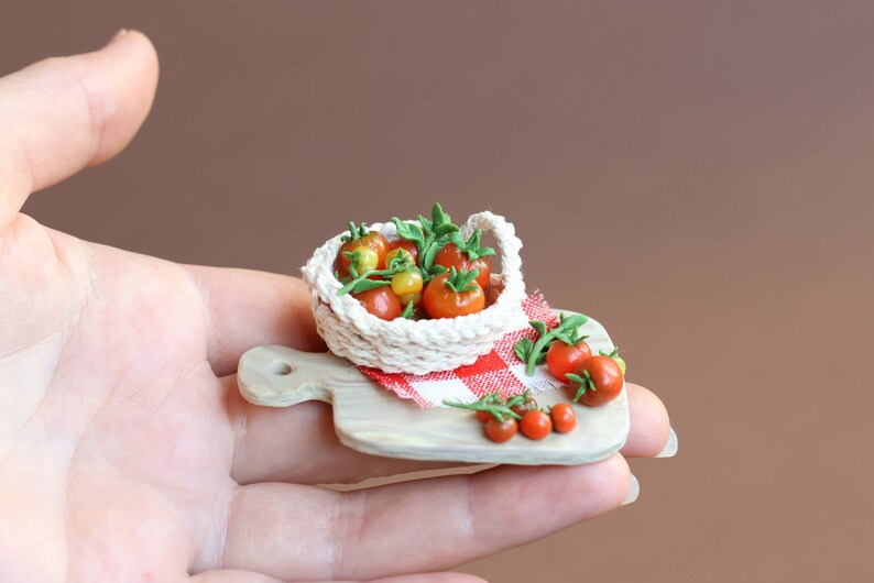 May include: A miniature white crocheted basket filled with red and yellow tomatoes on a small wooden cutting board with a red and white checkered cloth.
