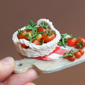 May include: A miniature white crocheted basket filled with red and yellow tomatoes, sitting on a wooden cutting board with a red and white checkered cloth. There are additional tomatoes scattered around the basket.