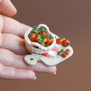 May include: A miniature wooden cutting board with a red and white checkered cloth, a small crocheted basket filled with red and yellow tomatoes, and additional tomatoes scattered around the basket.