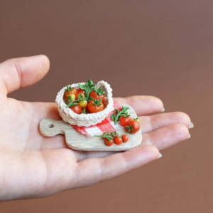May include: A miniature wooden cutting board with a red and white checkered cloth, a small white basket filled with red and yellow tomatoes, and a few loose tomatoes on the board.