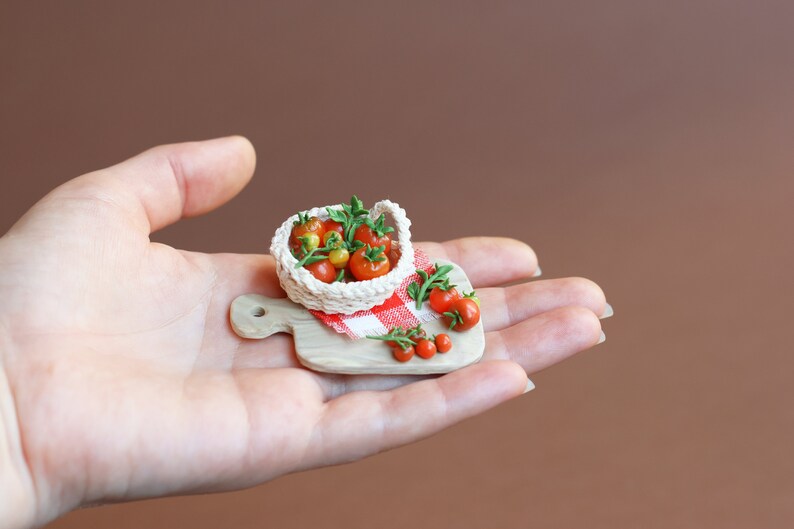 May include: A miniature wooden cutting board with a red and white checkered cloth, a small white basket filled with red and yellow tomatoes, and a few loose tomatoes on the board.