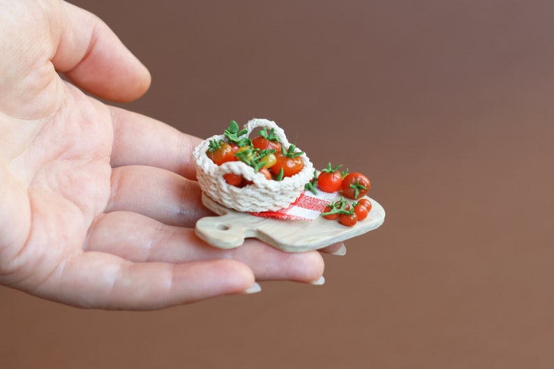 May include: A miniature wooden cutting board with a small crocheted basket filled with red and yellow tomatoes. A few extra tomatoes are scattered on the board.