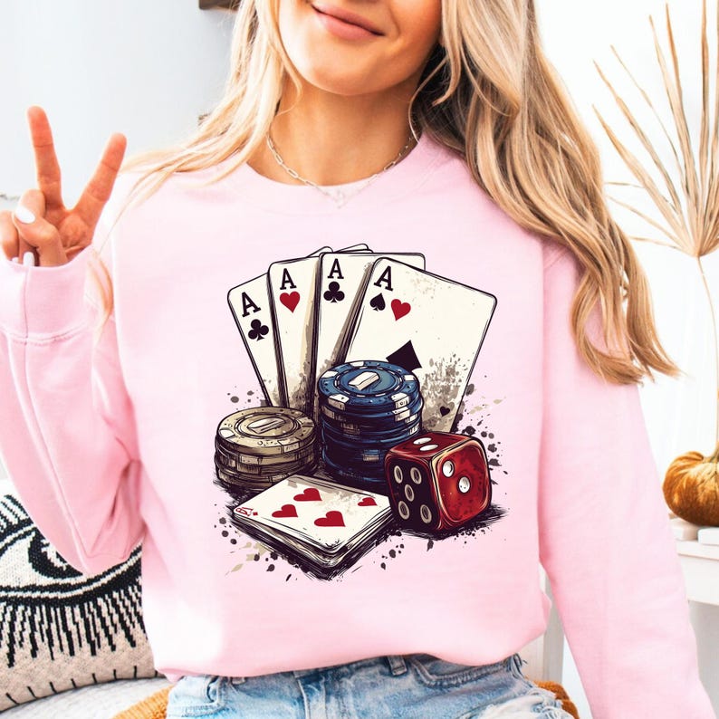 Puede incluir: Una sudadera rosa con un dise&ntilde;o gr&aacute;fico de cuatro ases, fichas de p&oacute;quer y un dado rojo. El dise&ntilde;o es de estilo vintage.