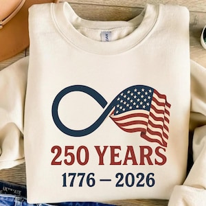 May include: Cream-colored sweatshirt featuring a navy blue infinity symbol intertwined with a waving American flag. The text "250 YEARS 1776-2026" is printed in red. A patriotic design celebrating a milestone anniversary.