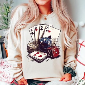 Puede incluir: Una sudadera blanca con un estampado gr&aacute;fico de cuatro ases, fichas de p&oacute;quer y un dado rojo. El gr&aacute;fico est&aacute; en un estilo vintage con un fondo descolorido.