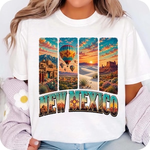 May include: A white t-shirt featuring a graphic print of four vertical panels depicting New Mexico landscapes, including adobe buildings, hot air balloons, desert dunes, and rock formations, with the text NEW MEXICO in a bold, colorful font.