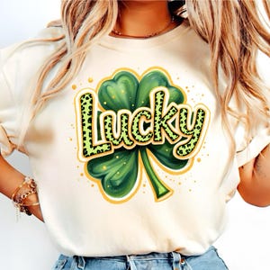 May include: A white t-shirt with a green four-leaf clover and the word "Lucky" in black and green letters with a leopard print pattern.