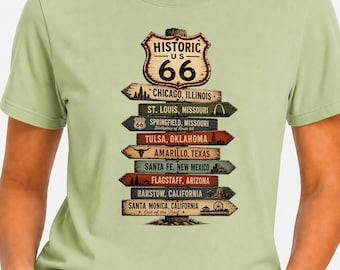 Puede incluir: Una camiseta verde claro con un gráfico de una señal de madera con el texto Historic US 66. La señal enumera ciudades como Chicago, St. Louis, Springfield, Tulsa, Amarillo, Santa Fe, Flagstaff, Barstow y Santa Monica junto con varios iconos.