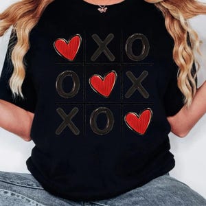 May include: Black t-shirt with a red heart and X's and O's in a tic-tac-toe board design.
