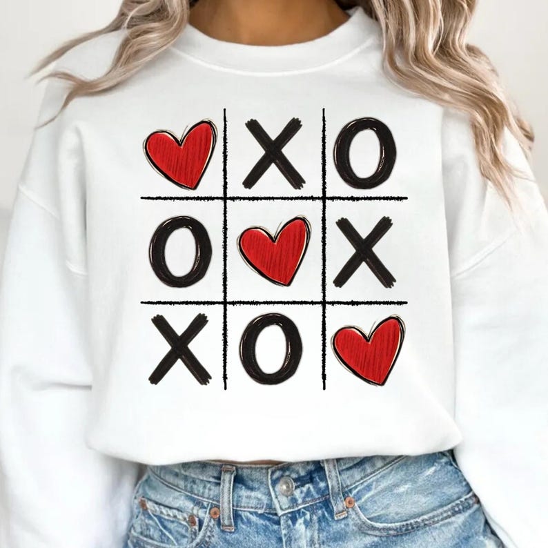 May include: White sweatshirt with a black and red tic-tac-toe design. The design features hearts and X's and O's.