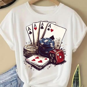Puede incluir: Camiseta blanca con un estampado gr&aacute;fico de cuatro cartas de juego, fichas de p&oacute;quer y un dado rojo. Las cartas son todas ases y el dado muestra un seis.