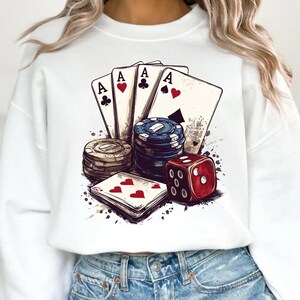 Puede incluir: Sudadera blanca con un estampado gr&aacute;fico de cuatro cartas de juego, una pila de fichas de p&oacute;quer y un dado rojo. Las cartas son todas ases y tienen un coraz&oacute;n rojo, una pica negra, un tr&eacute;bol negro y un diamante rojo.