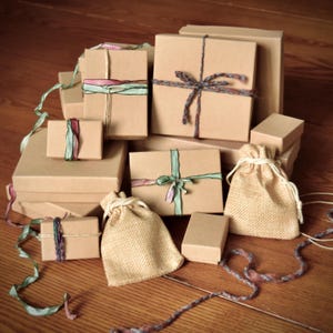 May include: A collection of various sized brown cardboard gift boxes and burlap pouches. The boxes are tied with colorful ribbons and twine. The gifts are arranged on a wooden surface.