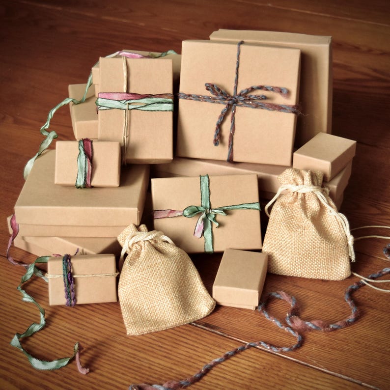 May include: A collection of various sized brown cardboard gift boxes and burlap pouches. The boxes are tied with colorful ribbons and twine. The gifts are arranged on a wooden surface.