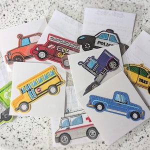 Op de afbeelding: Een verzameling geborduurde patches met verschillende voertuigen, waaronder een schoolbus, brandweerwagen, politieauto, ambulance, taxi en pick-up truck. Elke patch is kleurrijk en gedetailleerd.