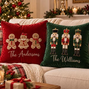 May include: Two square velvet throw pillows. The red pillow features three embroidered gingerbread cookies and the text The Andersons. The green pillow features three embroidered nutcracker figures and the text The Williams in white script.