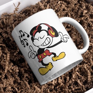 Puede incluir: Taza de caf&eacute; de cer&aacute;mica blanca con una imagen de dibujos animados de Mickey Mouse con auriculares y escuchando m&uacute;sica. La taza tiene un asa negra y el texto "Music" est&aacute; impreso en el lateral.