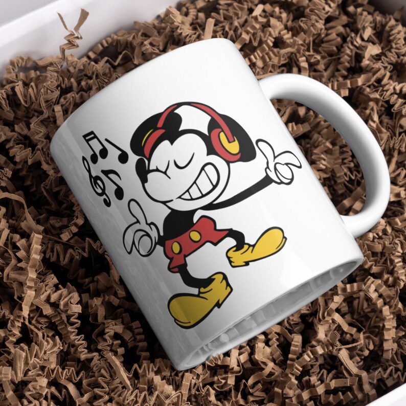 Puede incluir: Taza de caf&eacute; de cer&aacute;mica blanca con una imagen de dibujos animados de Mickey Mouse con auriculares y escuchando m&uacute;sica. La taza tiene un asa negra y el texto "Music" est&aacute; impreso en el lateral.