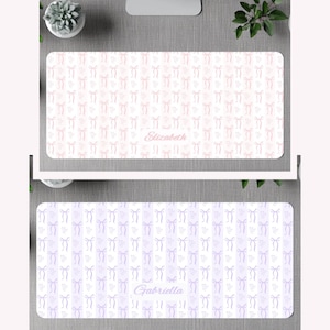 May include: Two rectangular desk mats featuring a repeating pattern of vertical stripes and small bows. The top mat is pink with the name Elizabeth printed in the center. The bottom mat is purple with the name Gabriella printed in the center.