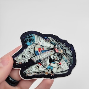 May include: A sticker featuring a detailed illustration of the Millennium Falcon spaceship against a dark blue space background. The spaceship is depicted in a dynamic pose, with its engines firing and its wings spread out.