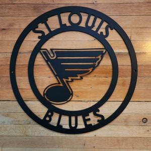May include: Black metal sign with the words "St. Louis Blues" in a circle. The Blues logo is a stylized note with a wing.