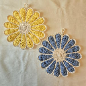 May include: Two round crochet potholders shaped like flowers. One potholder features yellow petals with a white center and border, while the other has blue petals with a white center and border. Each piece includes a small loop for hanging.