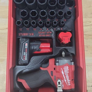 May include: A red Milwaukee Stubby 3/8 socket set 49-66-6801 in a red plastic carrying case. The set includes a red and black cordless impact wrench, a black M12 Redlithium XC4.0 battery, and various black metal sockets organized by size.