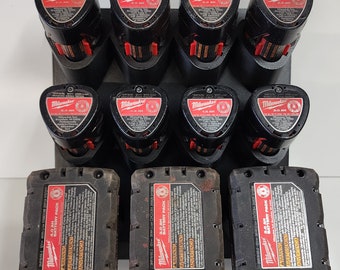 May include: A selection of black and red Milwaukee power tool batteries and battery packs. The batteries are displayed in a black holder. The batteries have labels with text and logos.