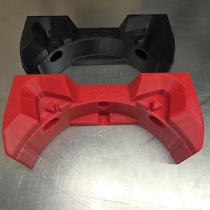 Peut inclure: Deux objets imprimés en 3D. Le supérieur est noir, et l'inférieur est rouge. Les deux ont un design incurvé et symétrique avec des bords arrondis et plusieurs trous circulaires. L'objet rouge porte l'inscription "TECHNIK3D".
