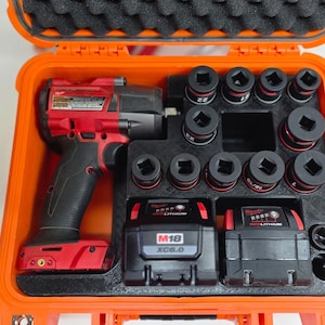May include: A bright orange hard-shell carrying case containing a red and black cordless impact wrench, two M18 REDLITHIUM XC6.0 battery packs, and a set of ten black impact sockets organised in a custom-fitted black foam insert.